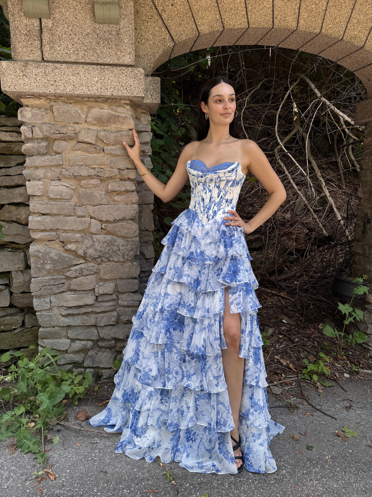 Woman in a blue and white patterned dress lying on a stone path with plants around.