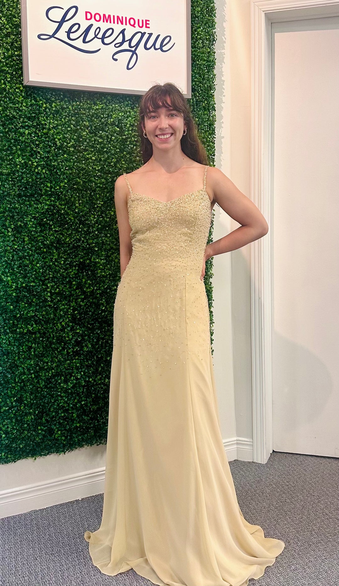 Woman in a yellow dress standing in front of a green wall with a sign that reads 'Dominique Levesque'.