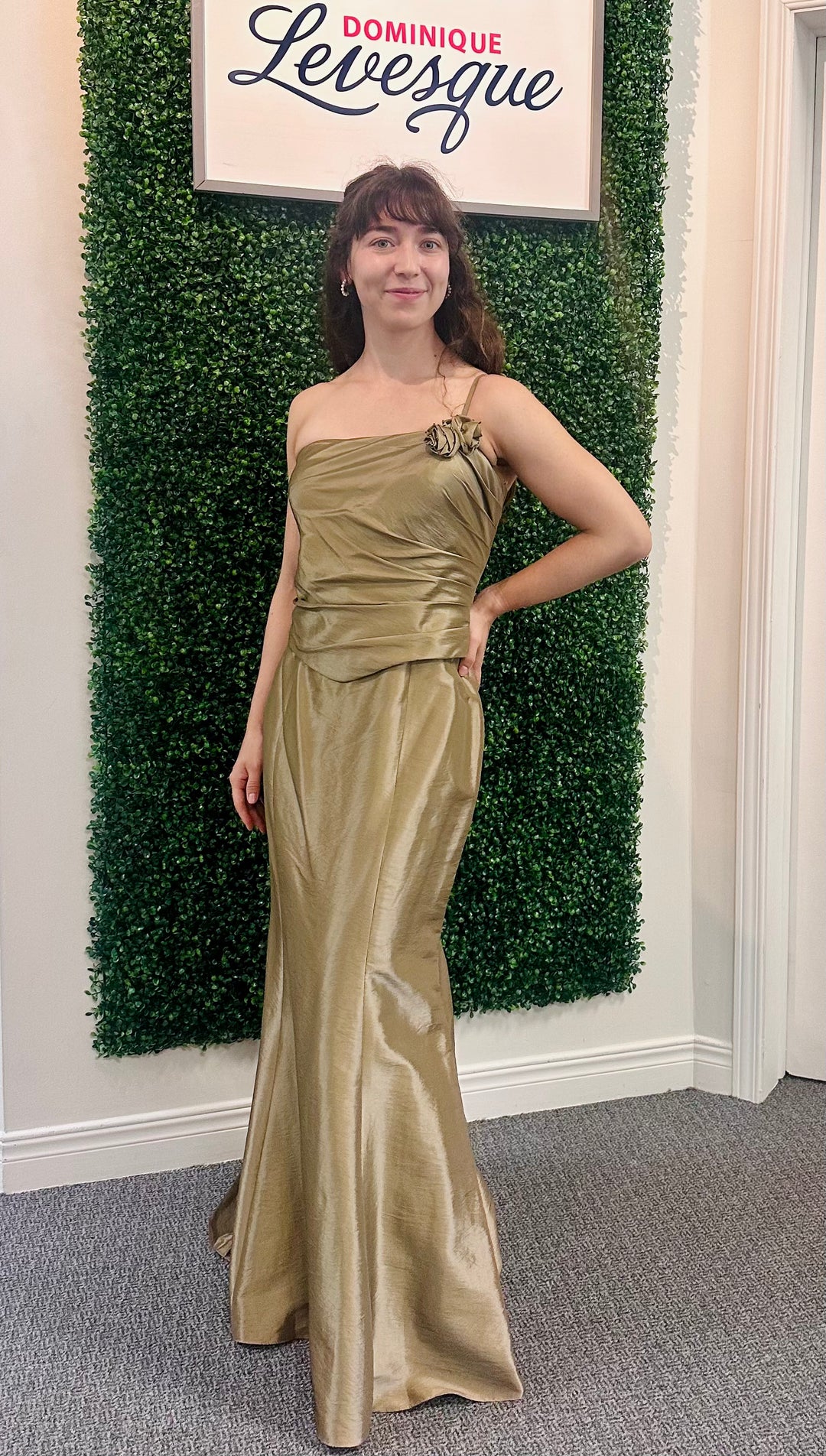 Woman in a olive dress standing in front of a green wall with a sign above it.