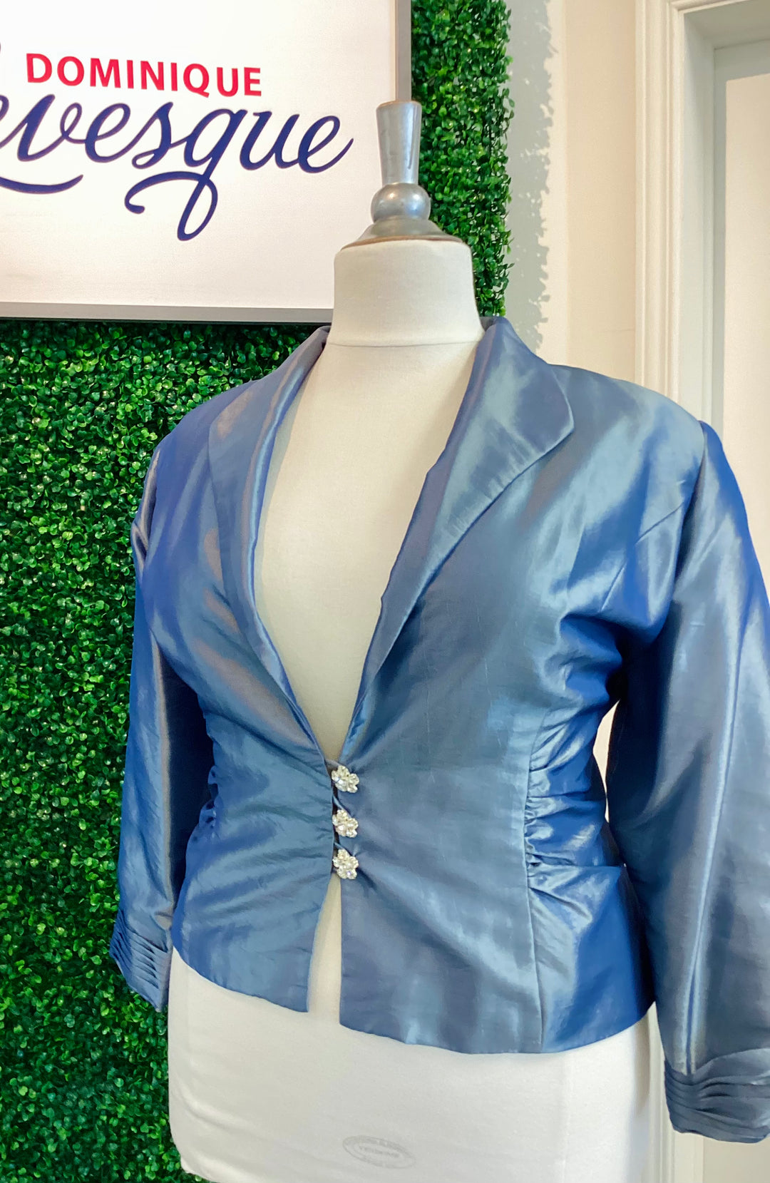 Blue jacket on a mannequin against a green leafy background with &