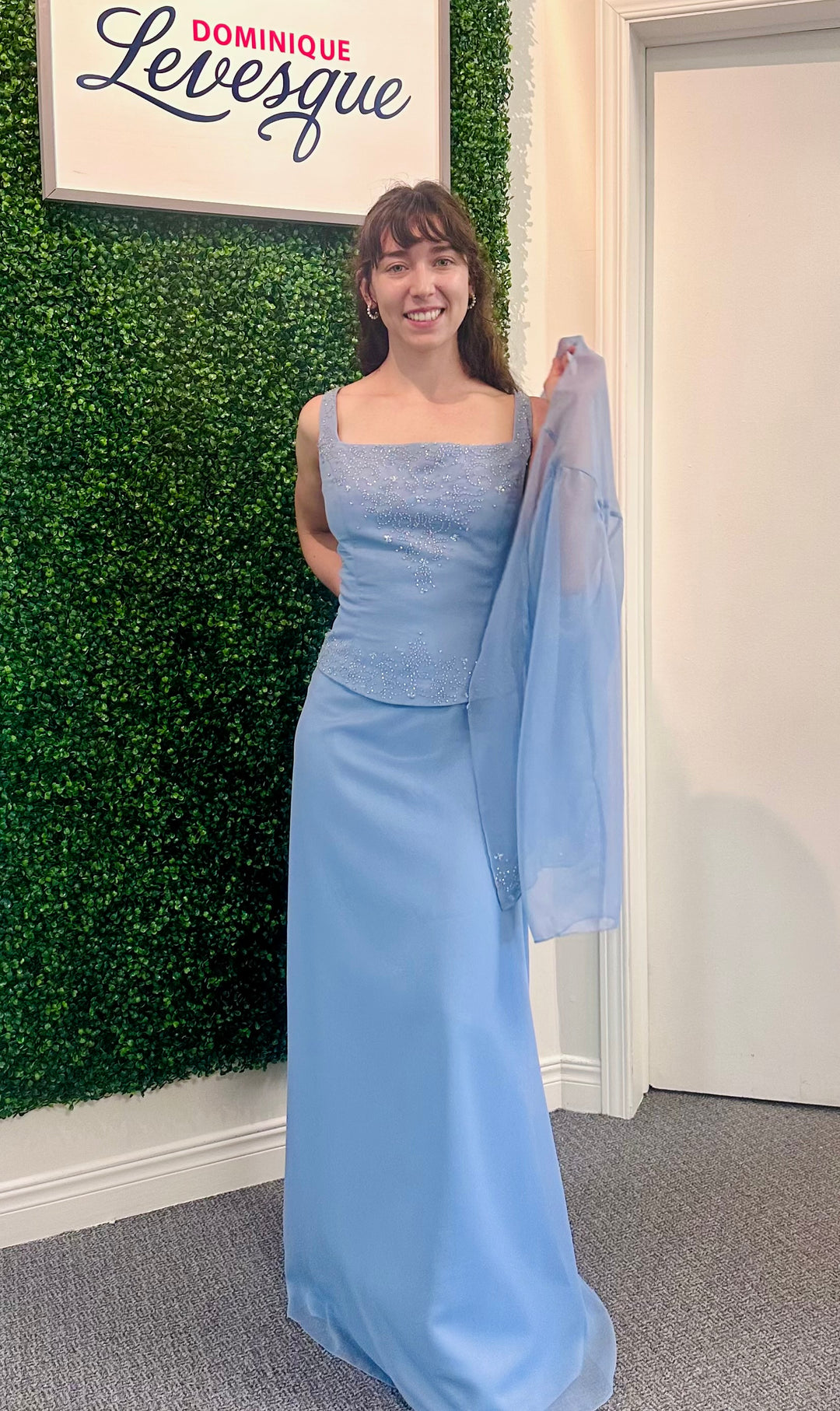 Woman holding a light blue dress in front of a green wall with &