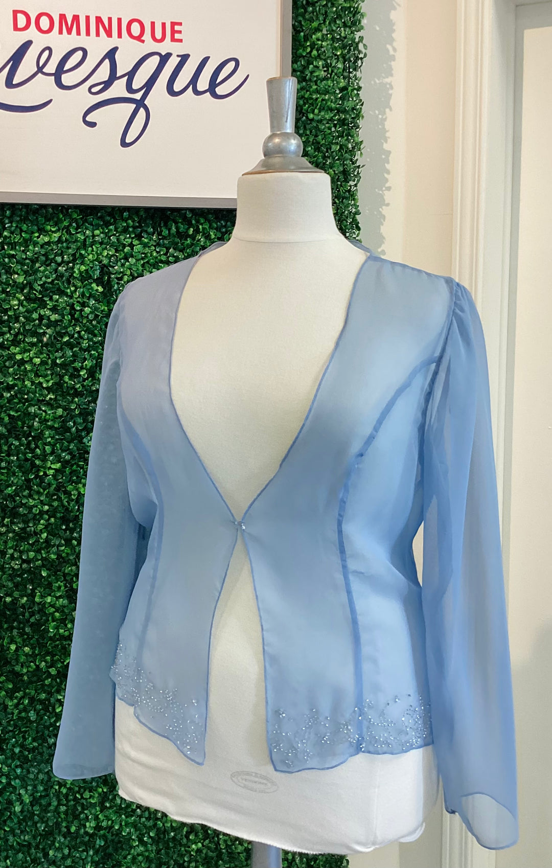 Light blue sheer jacket on a mannequin against a green leafy background with &
