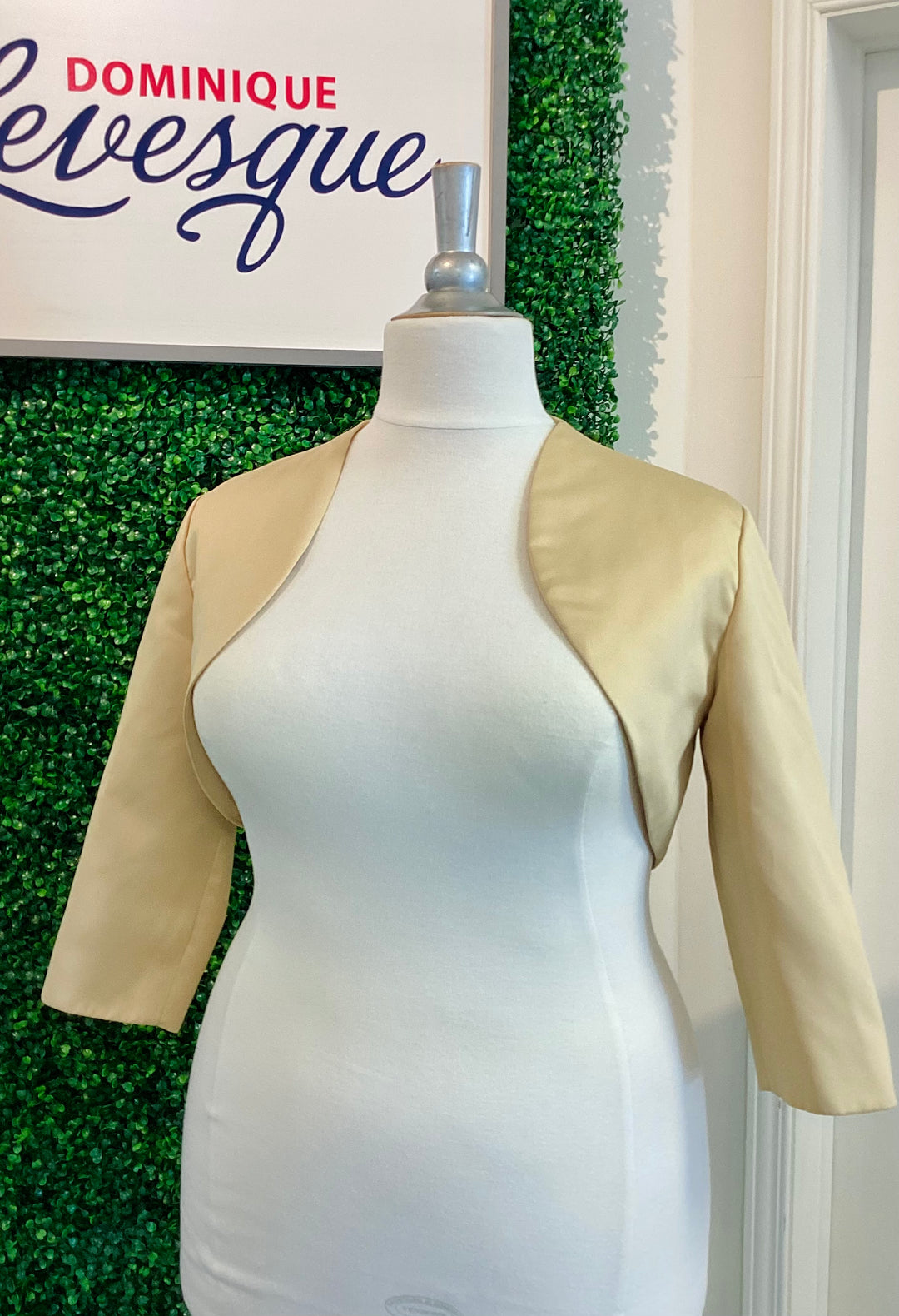 Mannequin wearing a beige jacket with a green leafy background and &