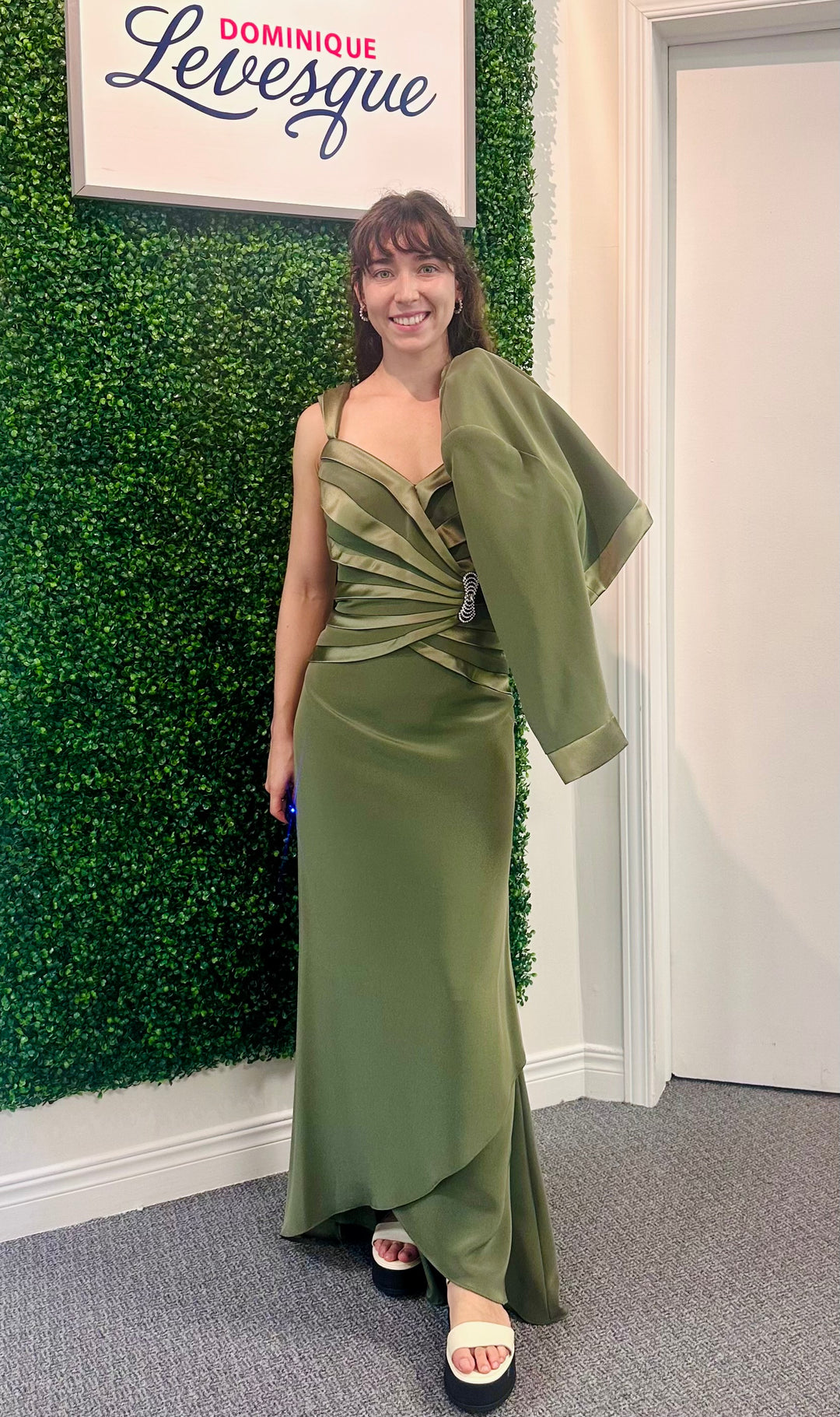 Woman in a green dress standing next to a green wall with a sign above it saying 'Dominique Levesque'.