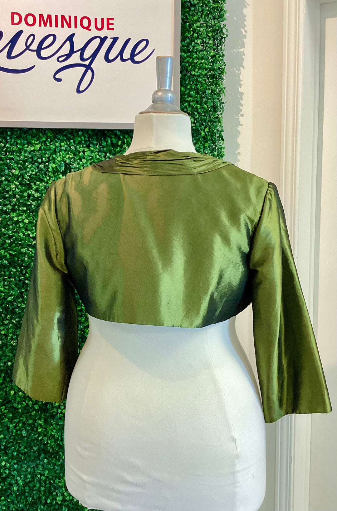 Olive satin bolero on a mannequin against a green leafy background with &