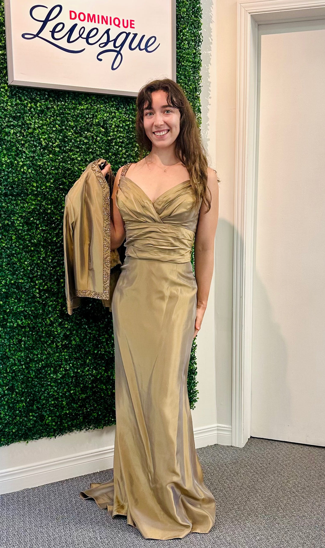 Woman in a gold dress standing against a green wall with a sign reading &