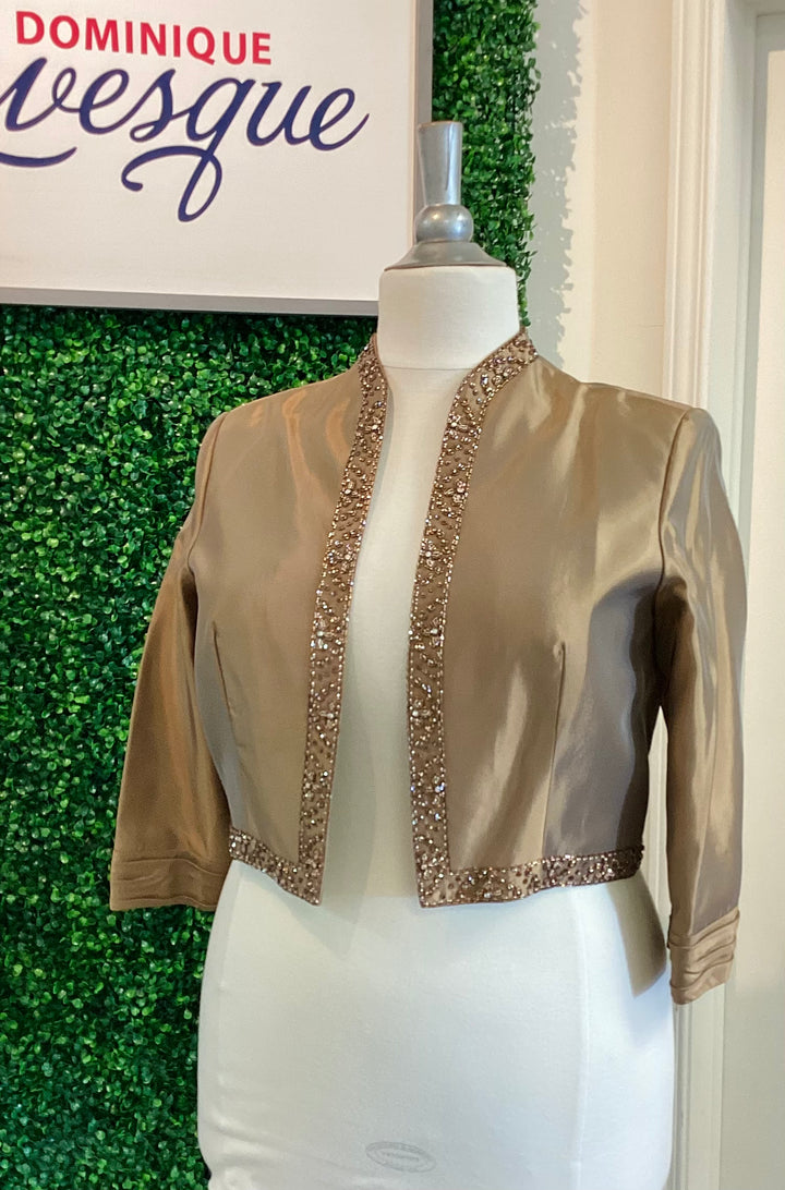 Bronze jacket with decorative trim on a mannequin against a green leafy background with &