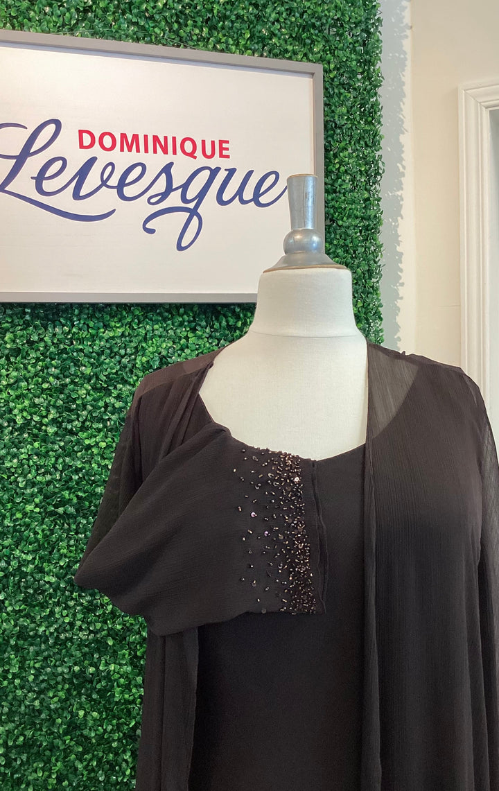 Mannequin wearing a brown dress with beaded details in front of a green leafy background and a sign reading &