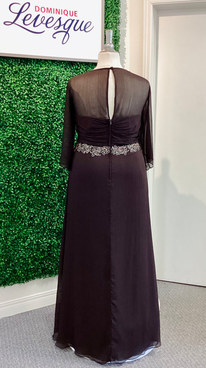 Chocolate evening gown with sheer overlay on a mannequin against a green leafy background.