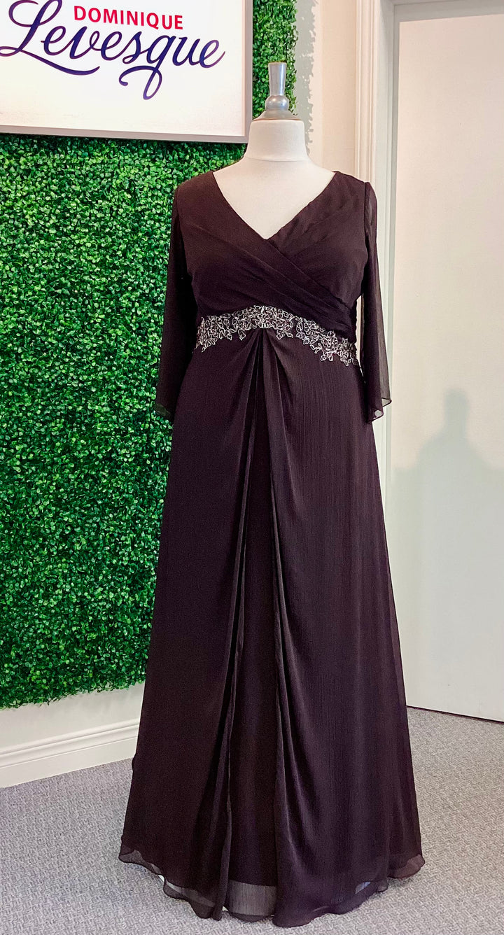 Dark brown evening gown with beaded waistband on a mannequin against a green leafy background.