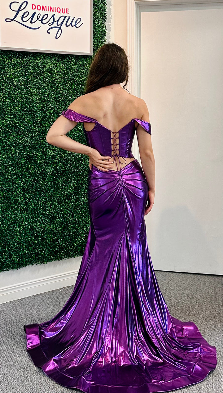 Woman in a purple off-shoulder gown with a high slit standing against a green leafy wall.