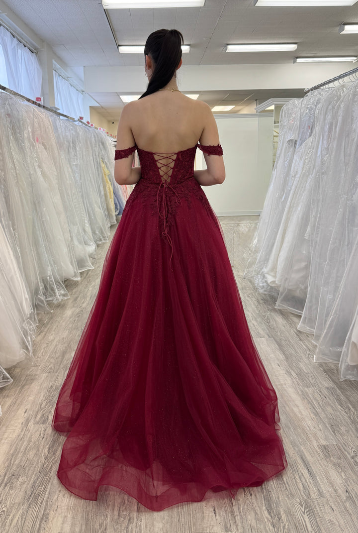 Woman wearing a burgundy evening gown in a fitting room with white gowns.