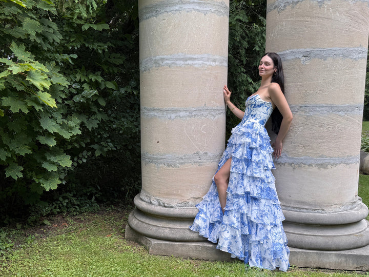 Woman in a floral dress standing between two stone columns in a garden setting