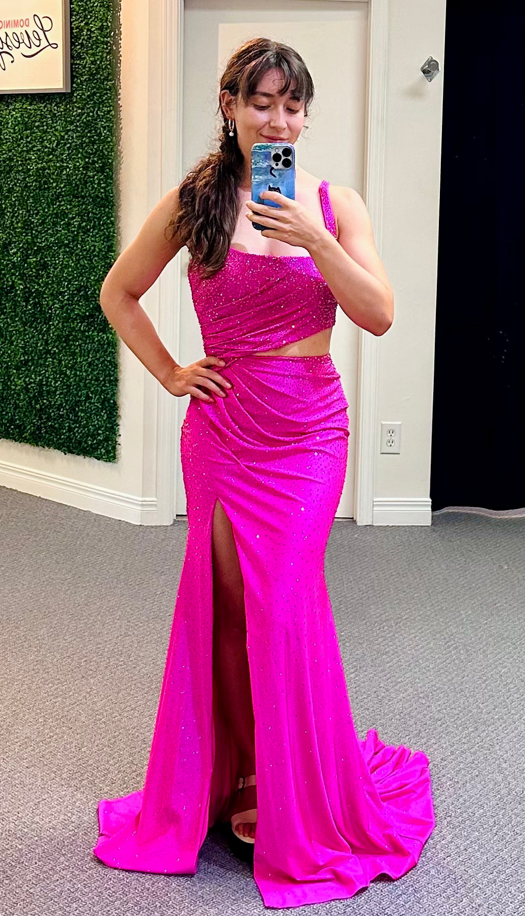 Woman wearing a bright pink dress with a slit, standing in a room with a green wall and a white door.
