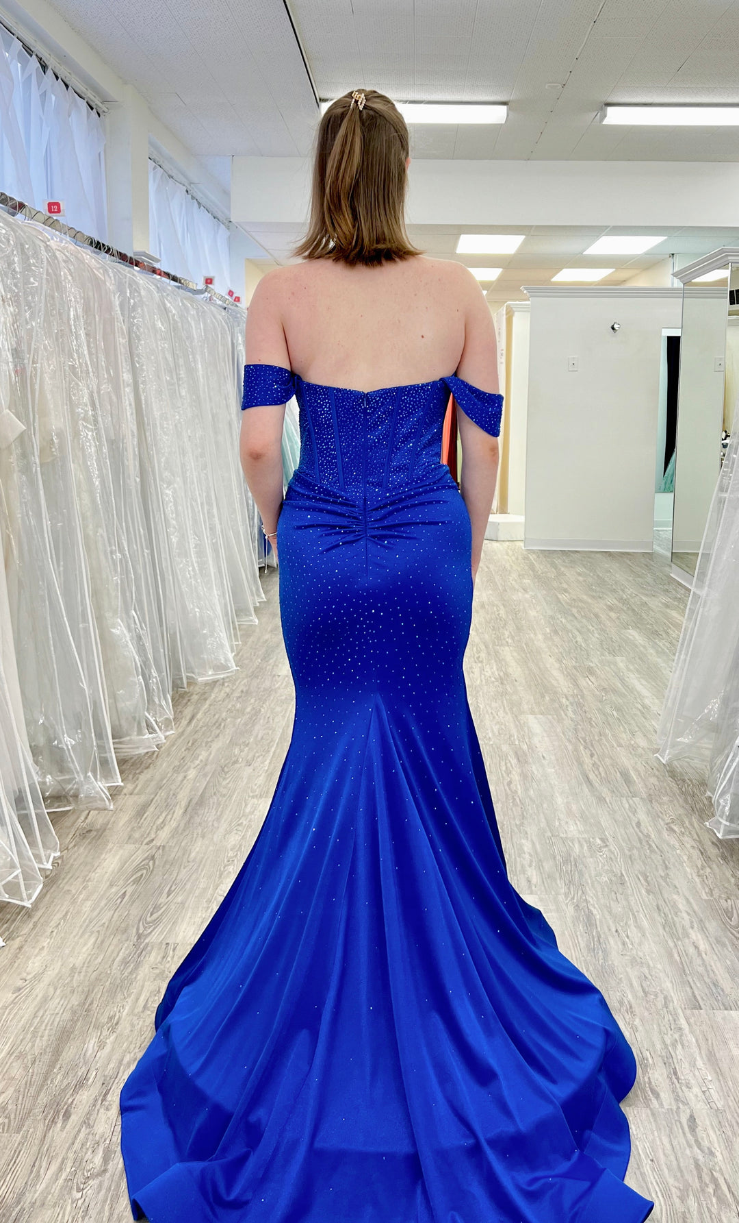 Women in a blue sparkly dress behind is the fitting room.