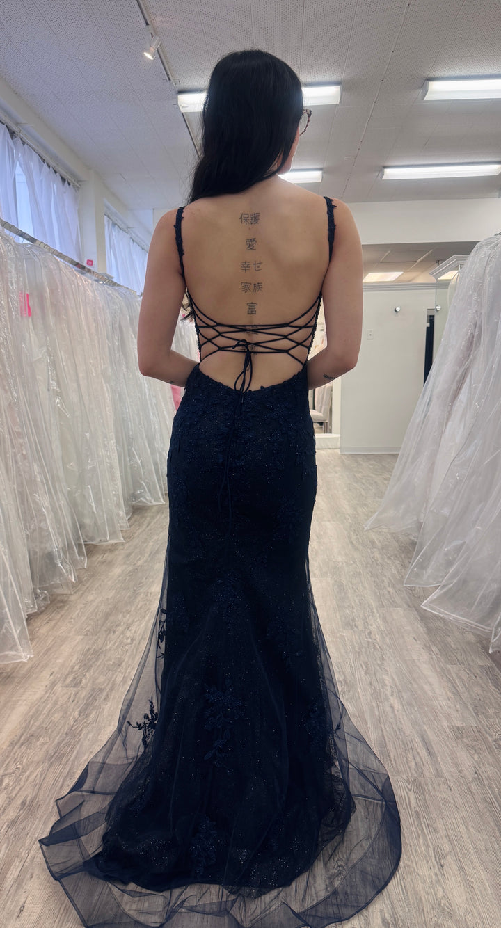 Person wearing a navy evening gown with intricate back design in a fitting room.