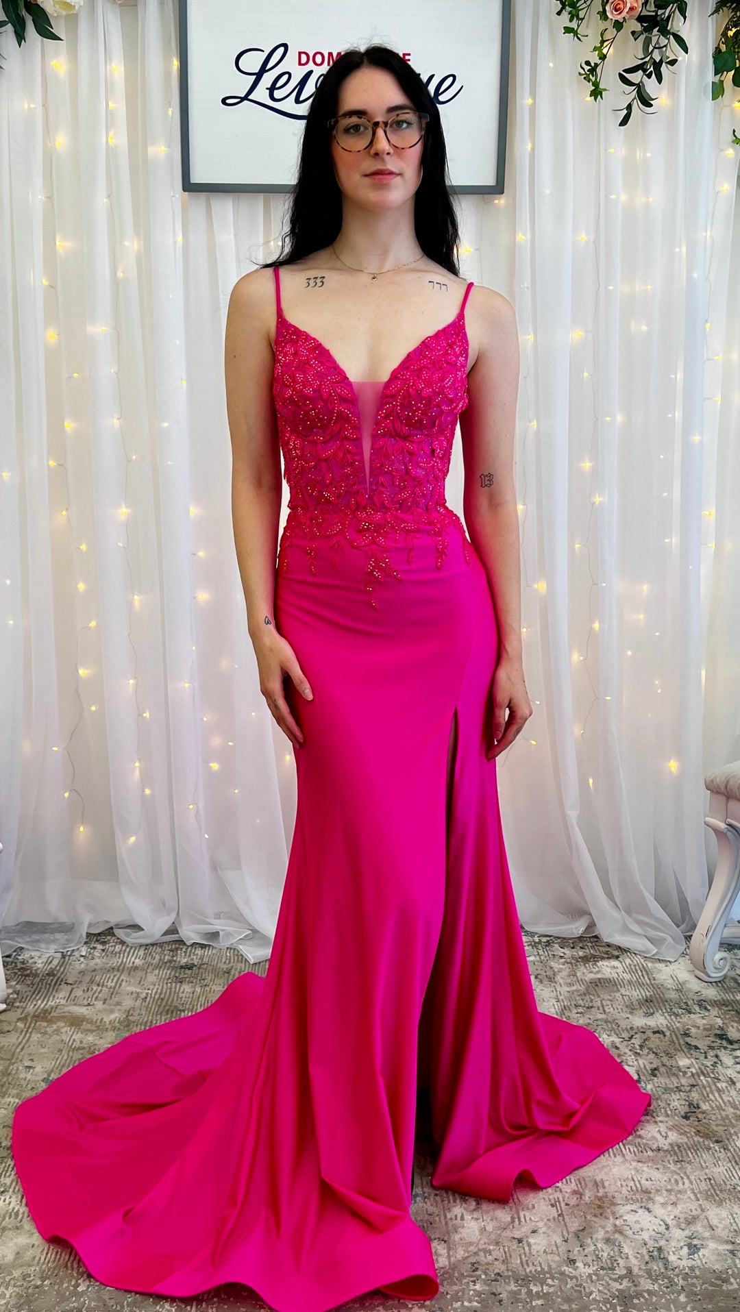 Woman wearing a fushia evening gown with a white curtain and decorative elements in the background