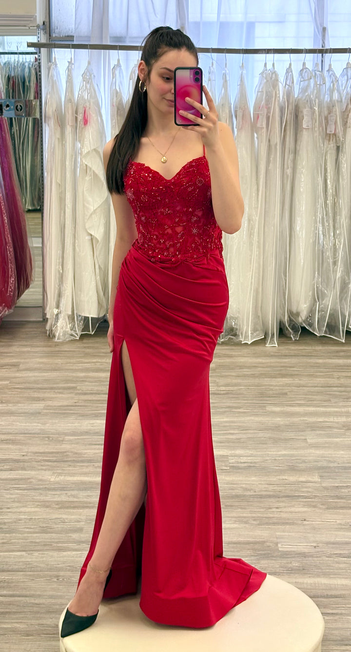 Woman in a red evening gown taking a mirror selfie in a fitting room.