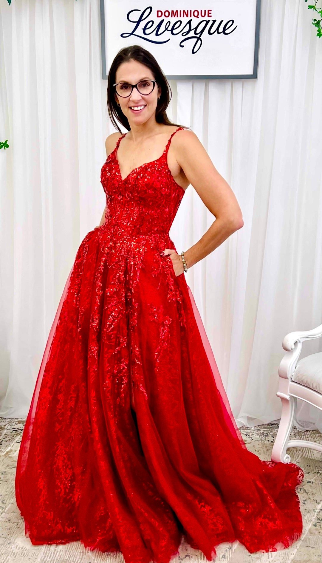 Woman wearing a red lace dress in a room with white curtains and a chair.