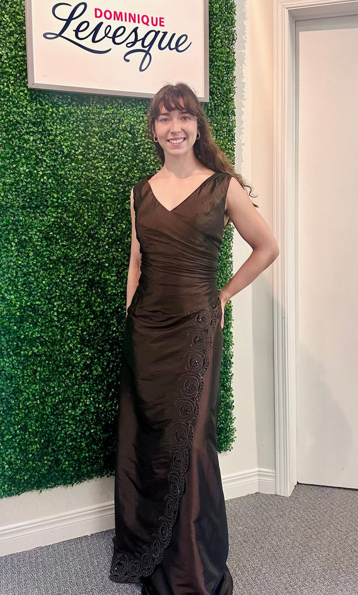 Woman in a brown evening gown standing against a green wall with a sign above saying &
