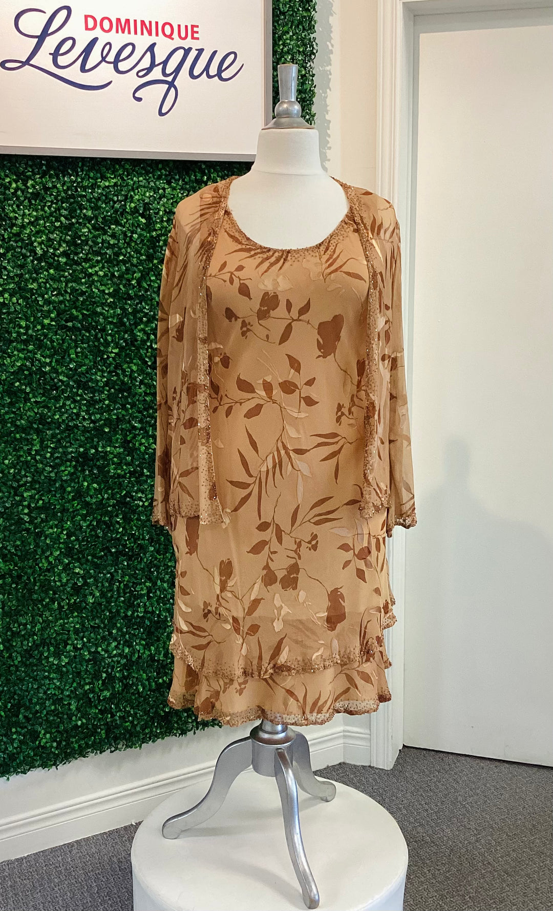 Bronze floral dress on a mannequin in front of a green wall with &