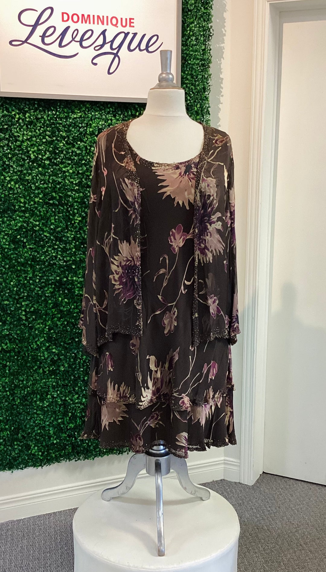Floral dress on a mannequin against a green wall with 'Dominique Levesque' branding.