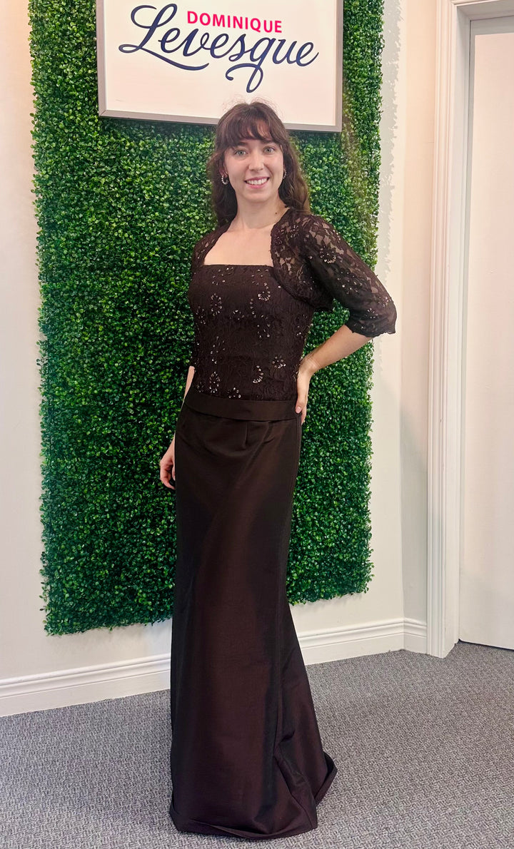 Woman in a brown evening gown standing in front of a green wall with a sign above saying &