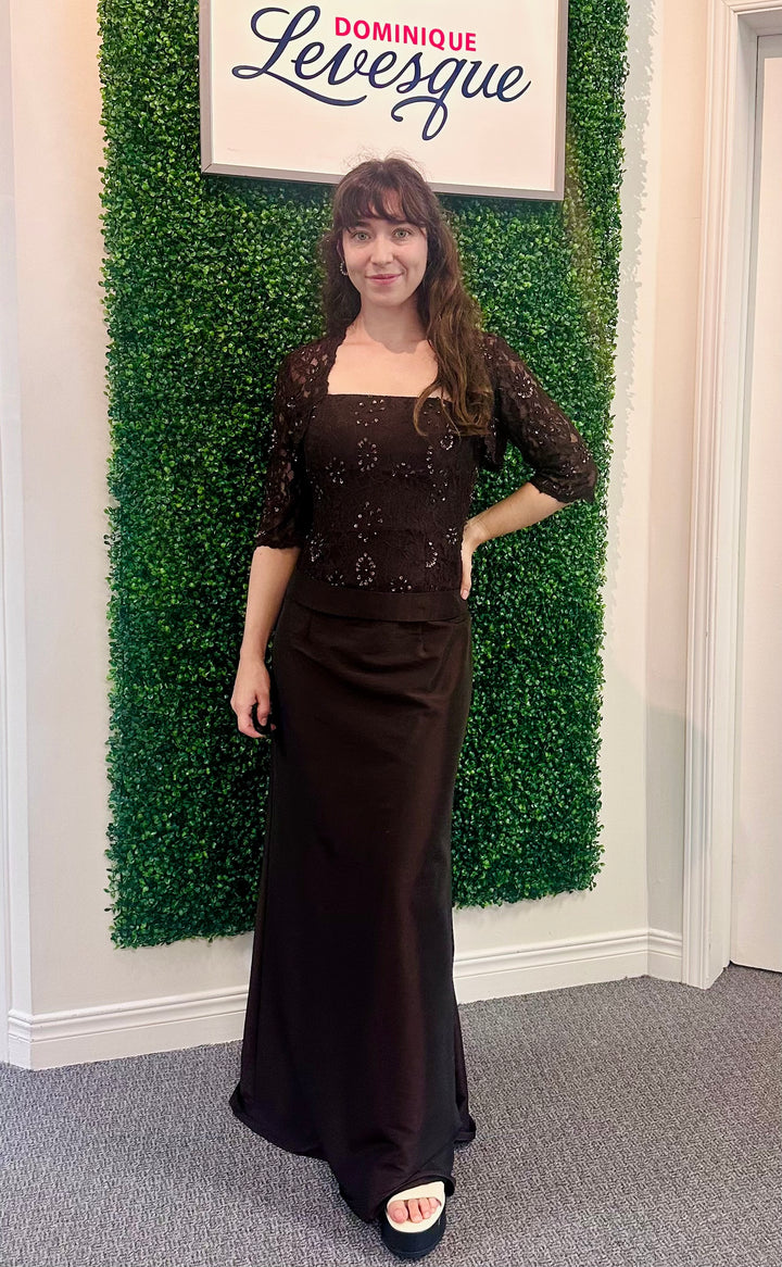Woman in a brown dress standing in front of a green wall with a sign above it saying &