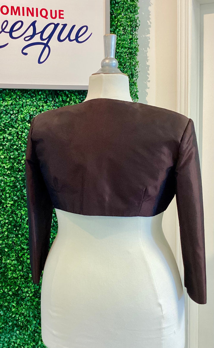 Brown bolero jacket on a mannequin against a green leafy background with &