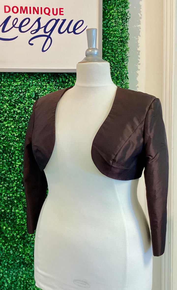 Brown shrug on a mannequin against a green leafy background with &