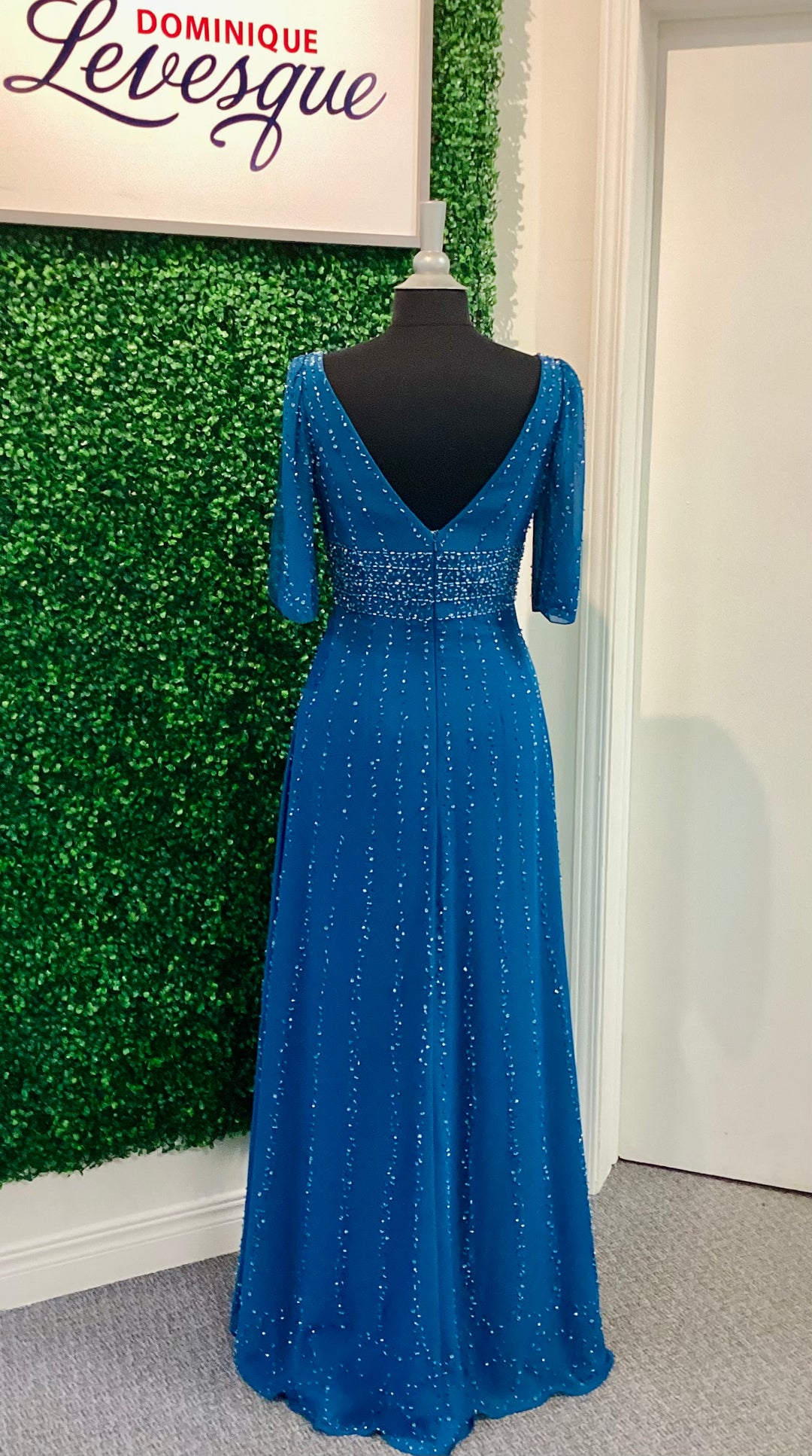 Blue evening gown on a mannequin against a green wall with &