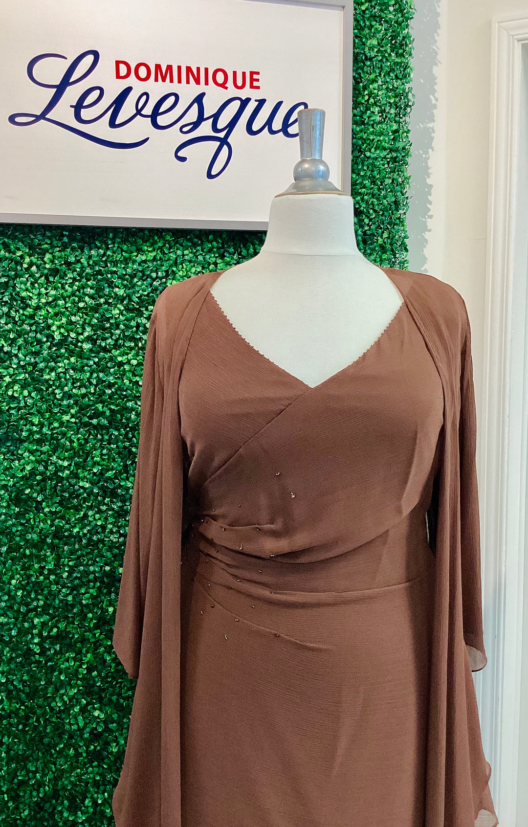 Brown dress on a mannequin against a green leafy background with &