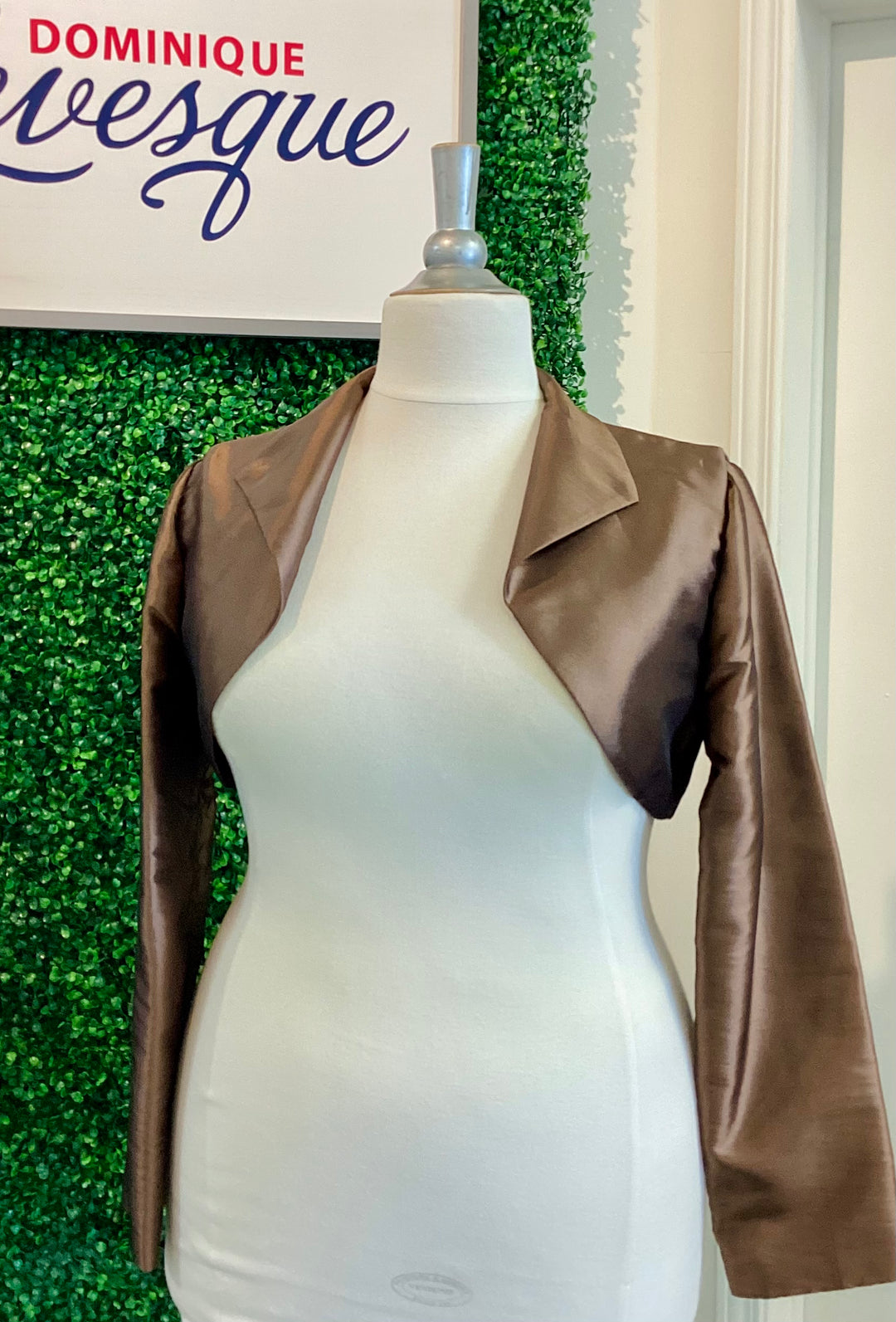 Brown leather jacket on a mannequin against a green leafy background with &
