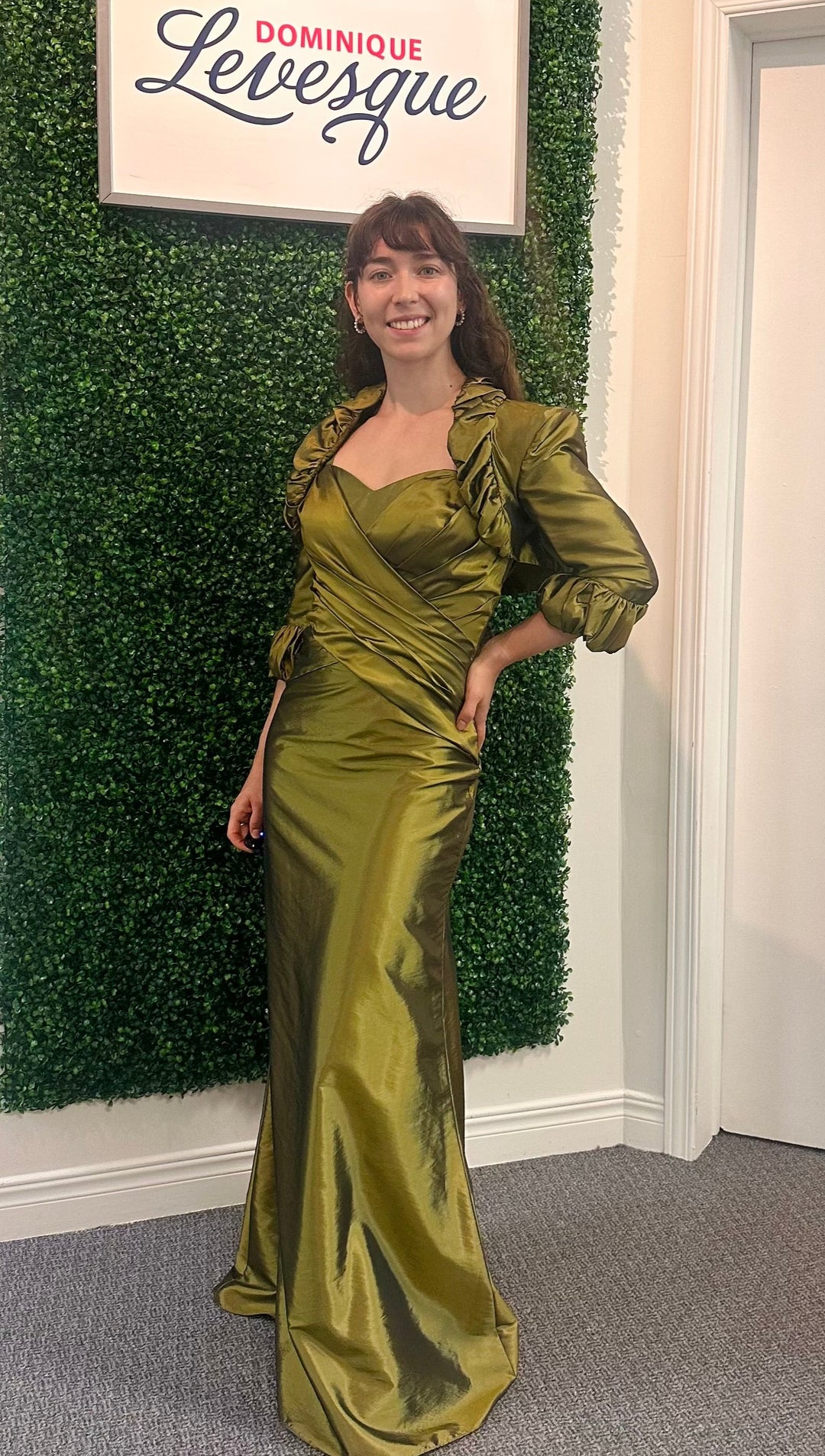 Woman in a green dress standing in front of a green wall with a sign above saying Dominique Levesque.