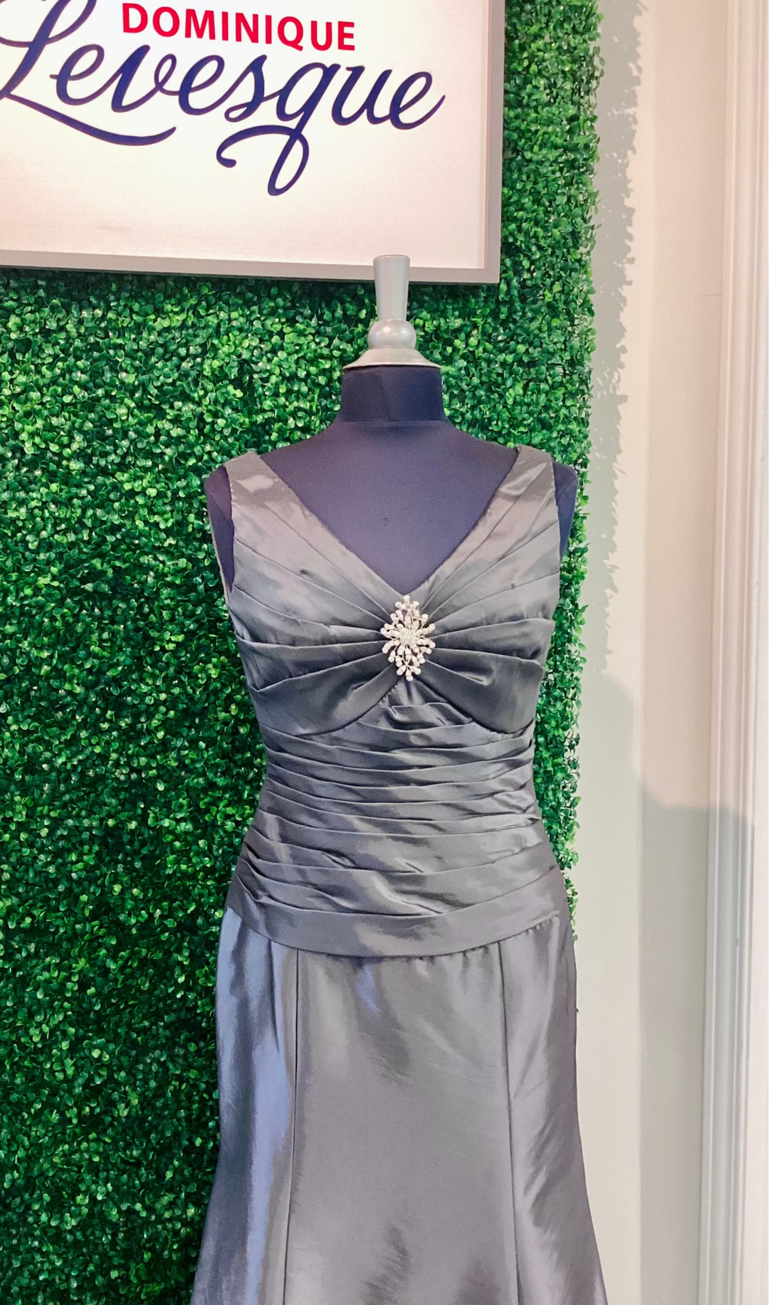 Gray evening gown on a mannequin against a green leafy background with &