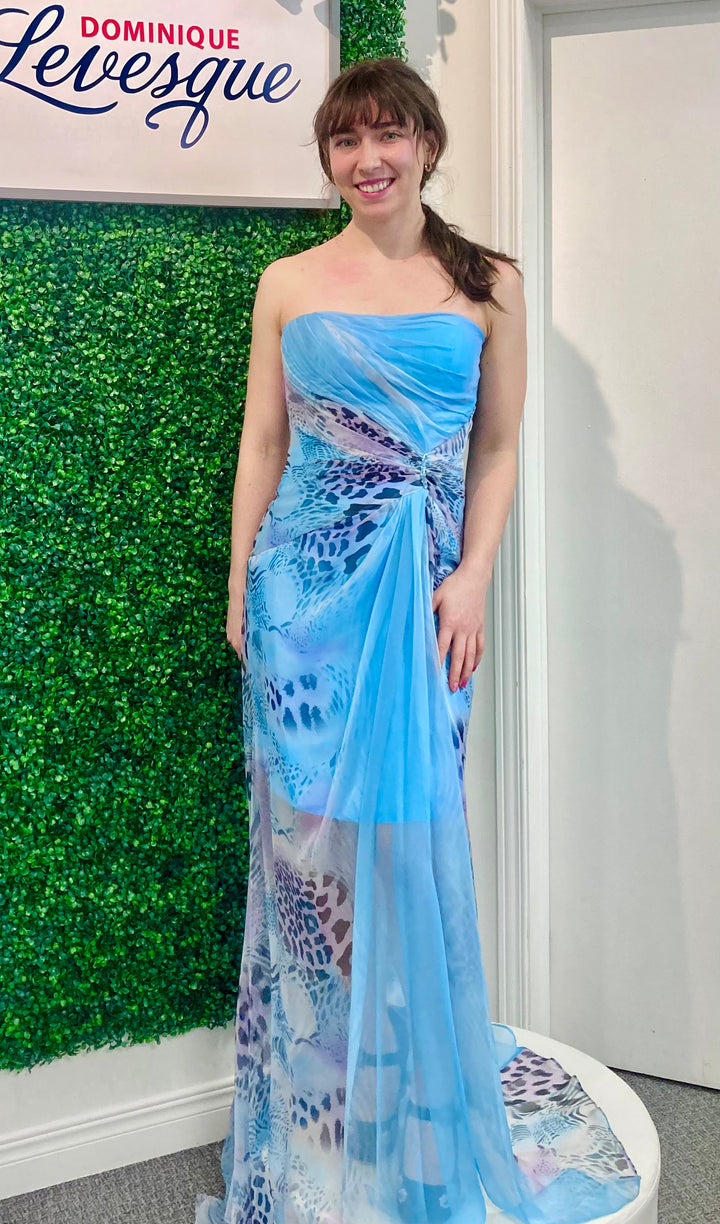 Woman wearing a turquoise strapless dress with floral patterns in front of a green wall and white door.