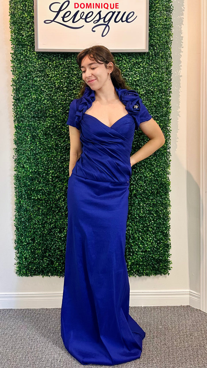 Woman in a purple evening gown standing against a green leafy wall with &