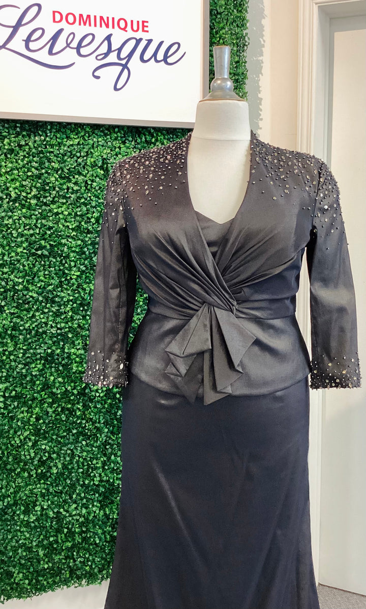 Black strapless gown with vest on a mannequin against a green leafy background with &