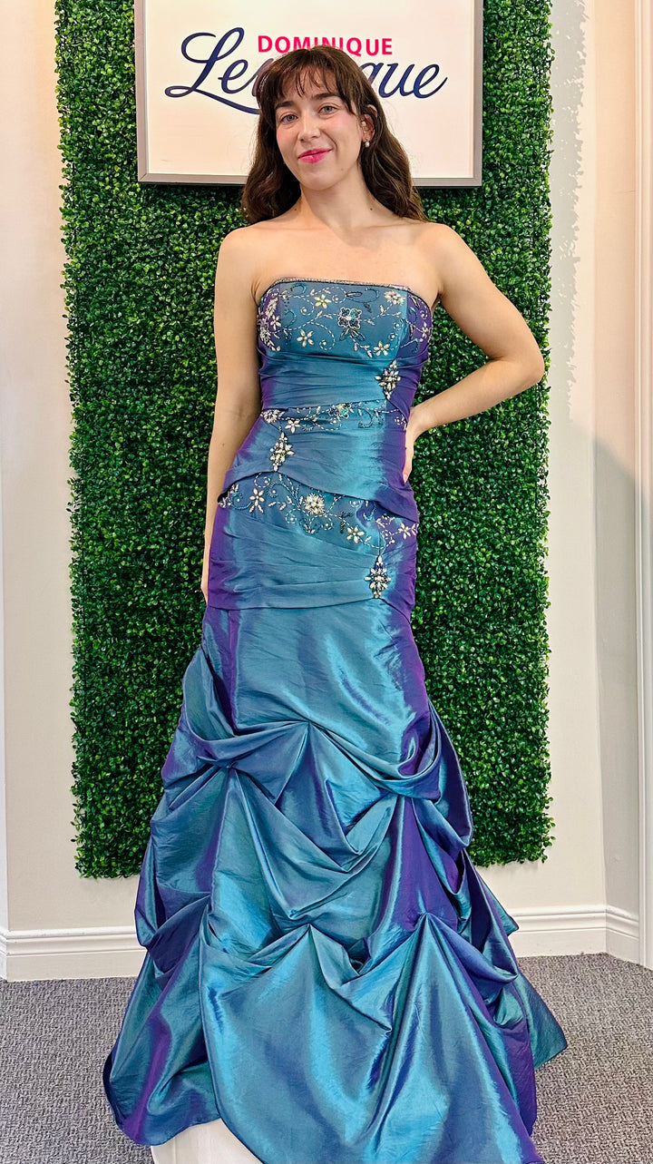 Woman in a blue and purple strapless gown posing in front of a green wall with a sign.