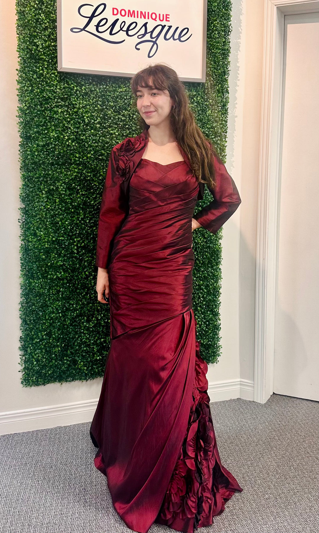 Woman in a burgundy evening gown standing in front of a green wall with &