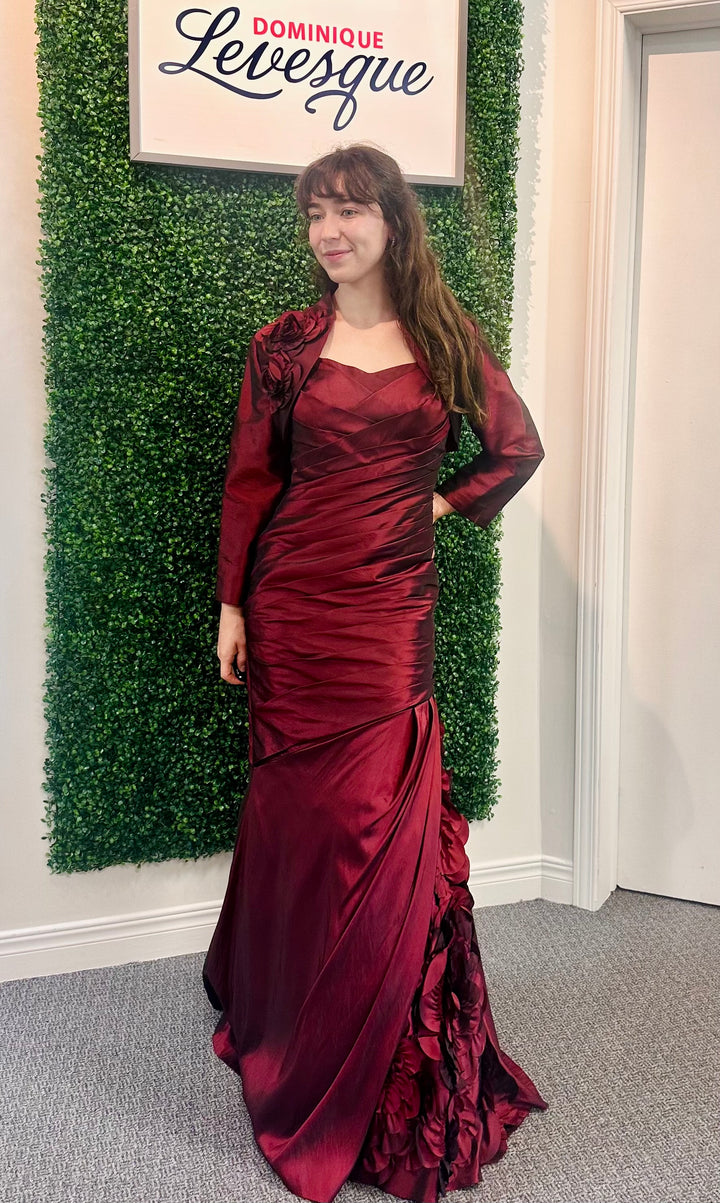 Woman in a burgundy evening gown standing in front of a green wall with &