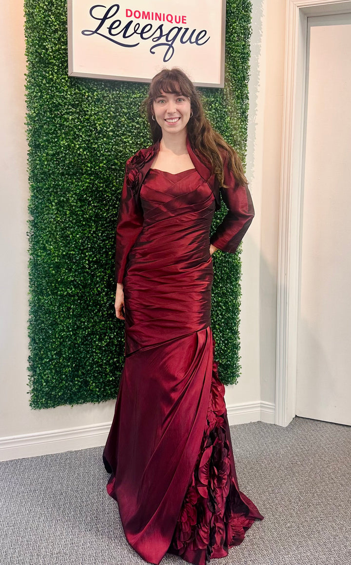 Woman in a burgundy evening gown standing in front of a green wall with &