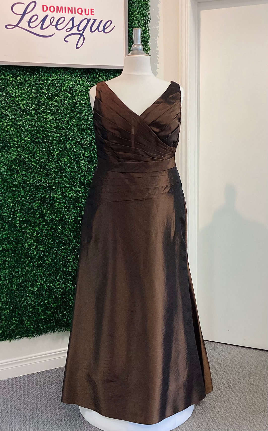 Cocoa evening gown on a mannequin against a green leafy background with &