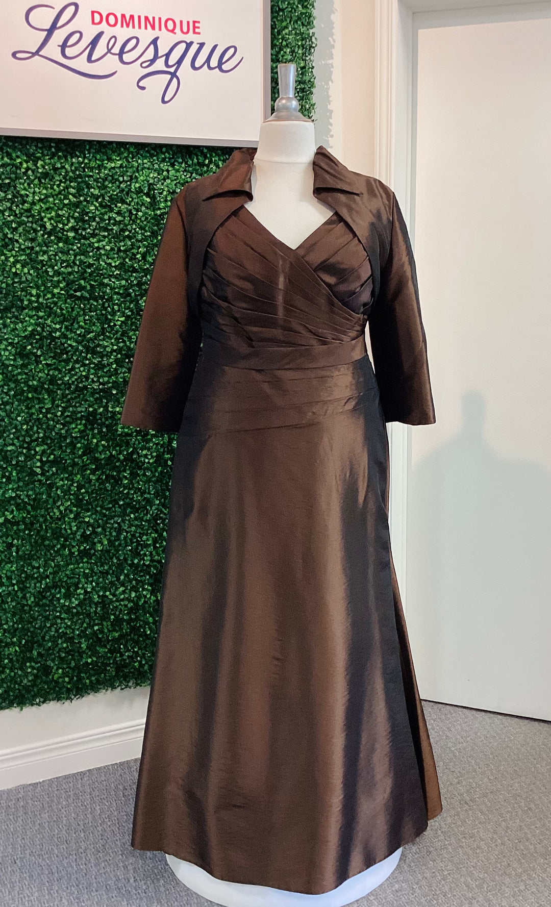 Cocoa dress on a mannequin with a green leafy background and 'Dominique Levesque' sign.