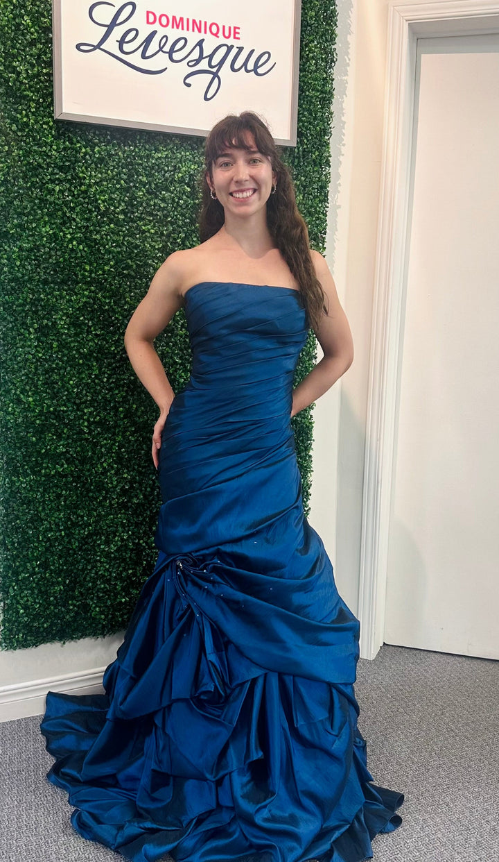Woman in a blue strapless gown standing in front of a green wall with a sign above it.