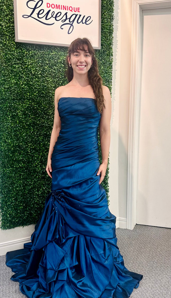 Woman in a blue strapless gown standing against a green leafy wall with &