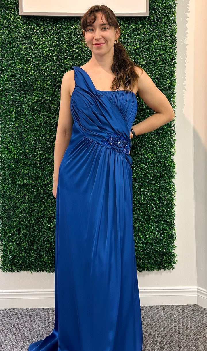Woman in a blue one-shoulder dress standing against a green leafy background