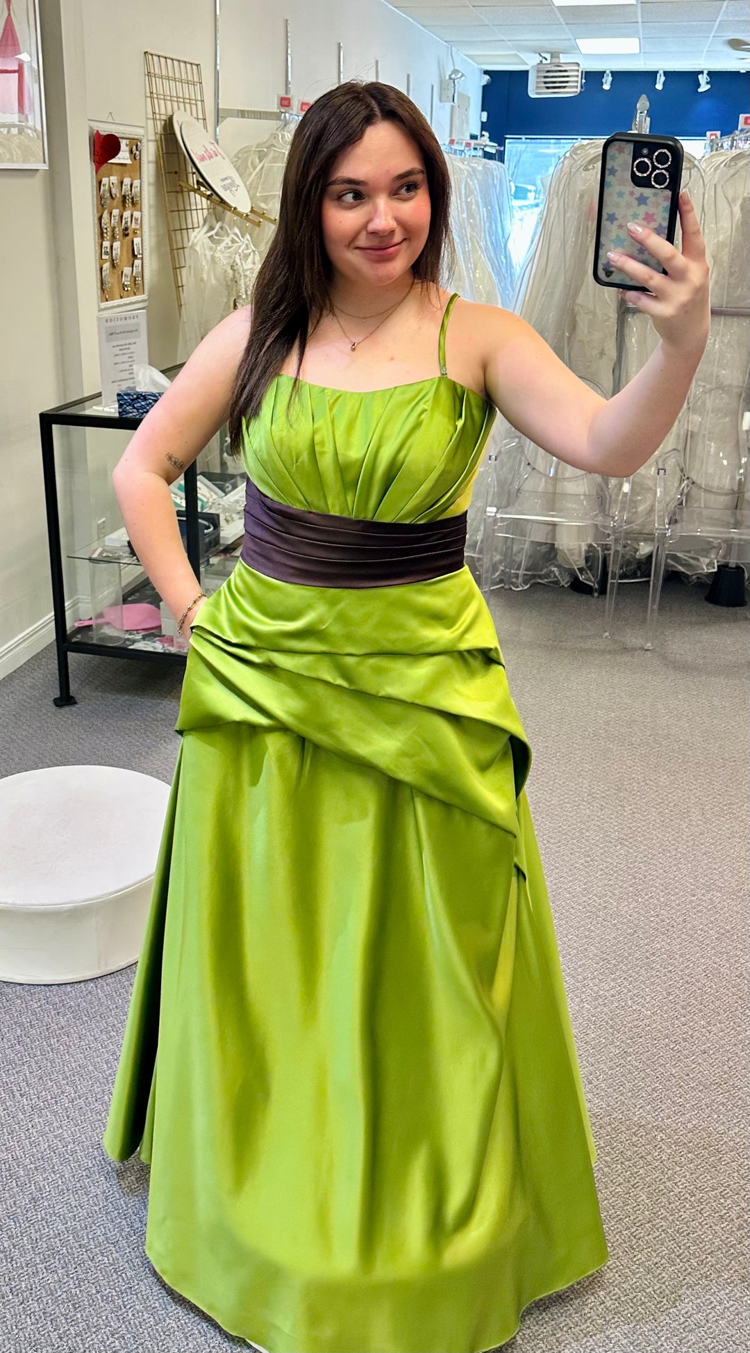 Woman taking a mirror selfie wearing a green dress with a brown belt in an indoor setting.