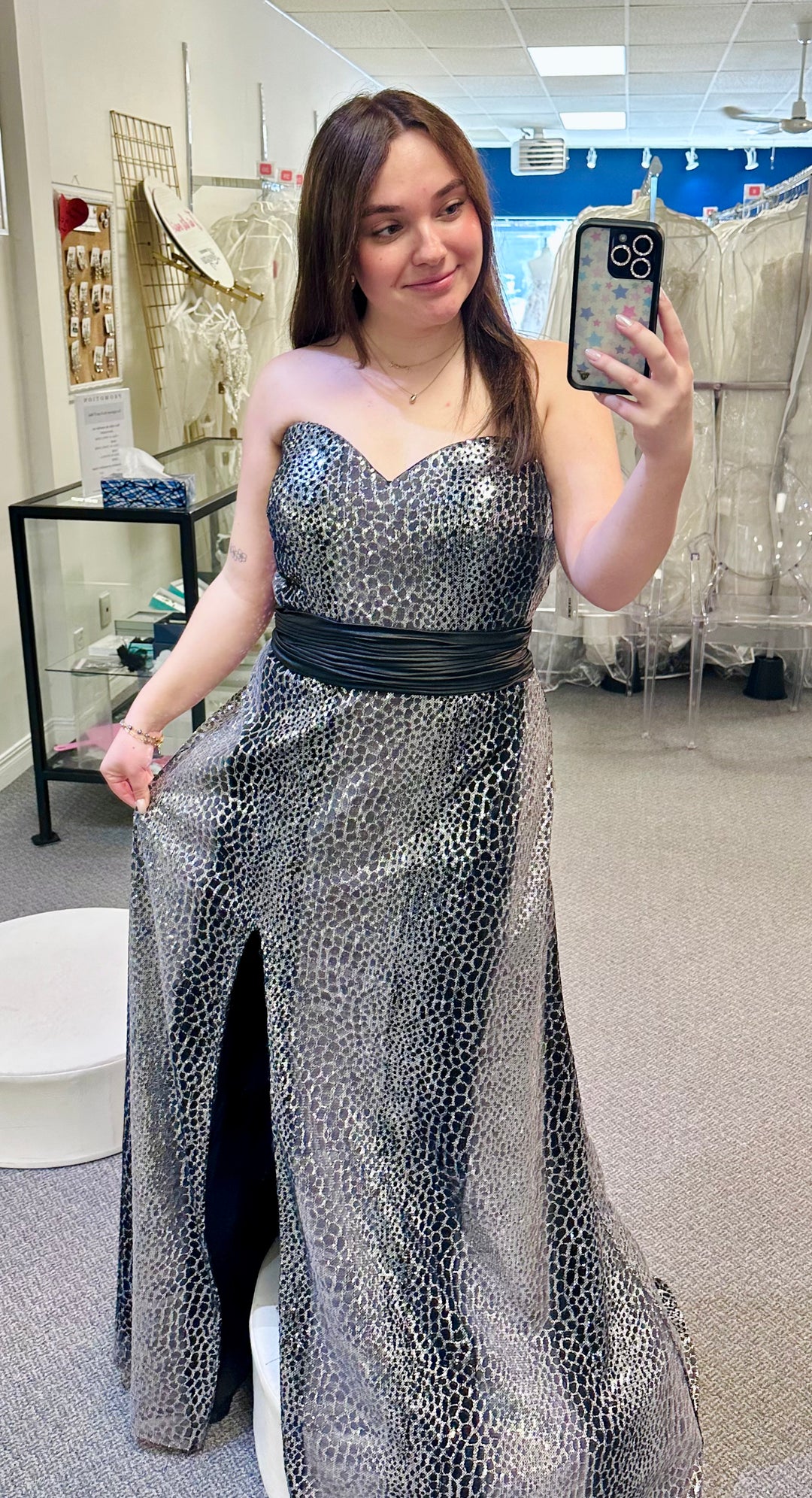 Woman in a silver sequin dress taking a mirror selfie in a store.