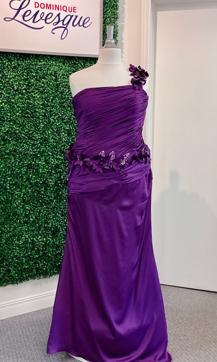 Purple evening gown on a mannequin against a green leafy background with &